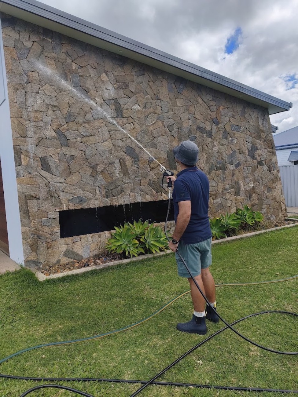 A man washing down the stone wall of a house with a hose