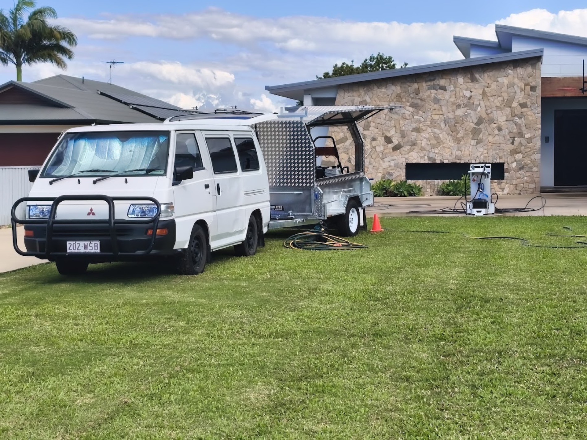 A work van and trailer parked on the grass in front of a stone-fronted house