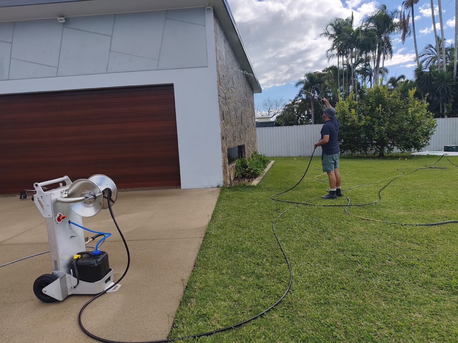 A man spraying water across a back lawn with the wash gear set up beside the house
