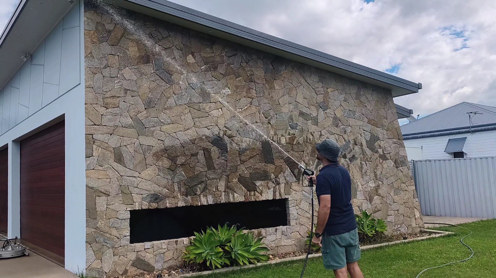 A man spraying water across the stone feature wall of a house
