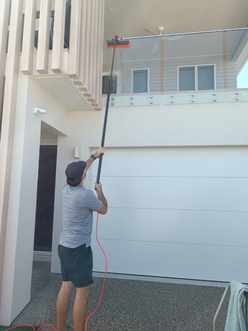 A man using a water-fed pole on the wall and window of a house