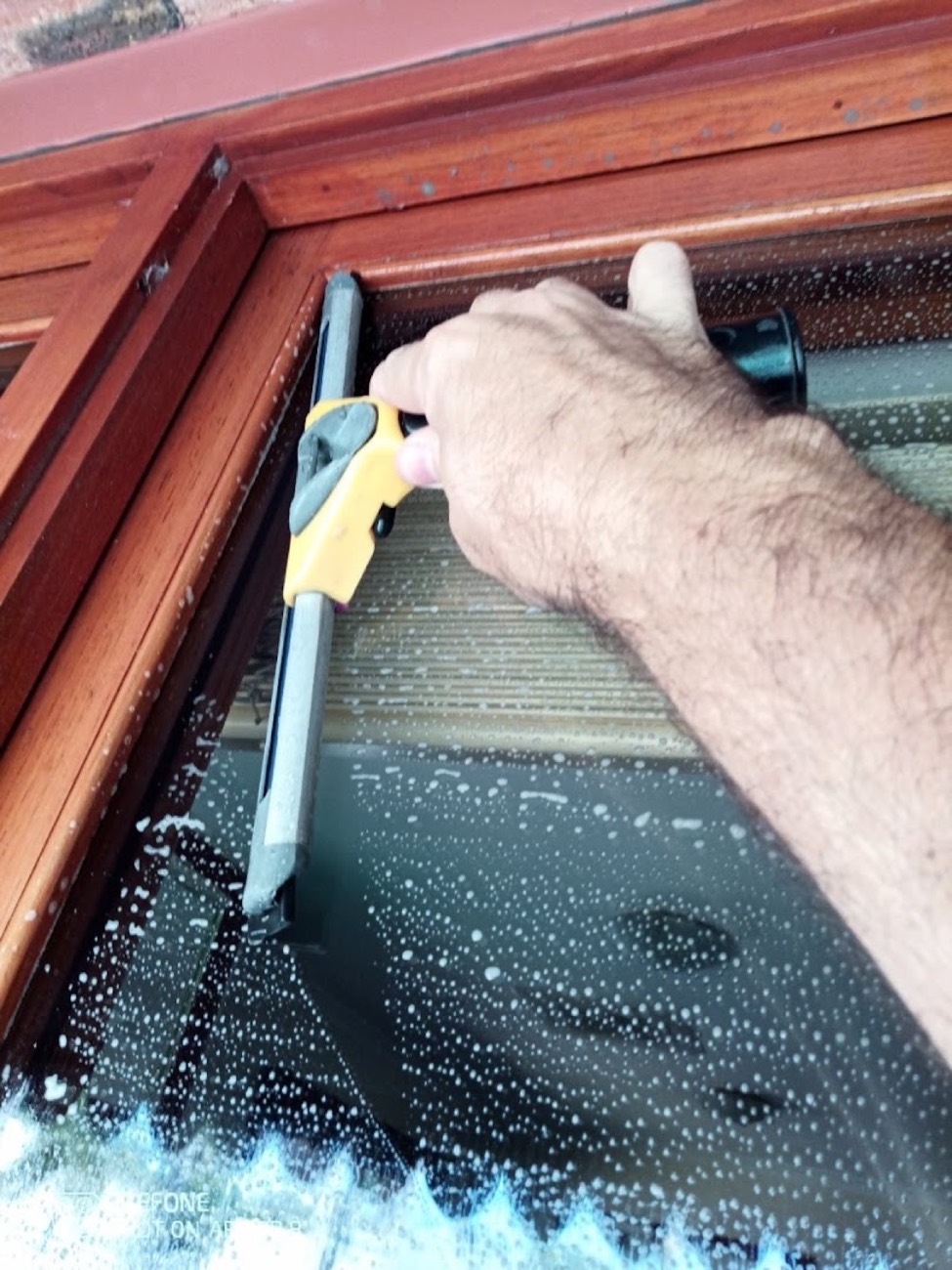 A hand drawing a squeegee down a soapy pane of glass