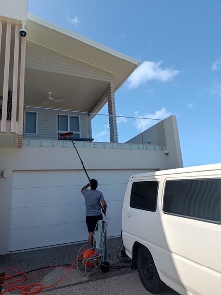 A man using a water-fed pole on the eaves of a house beside a van