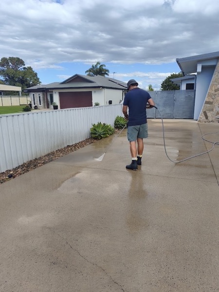 A man spraying water across a driveway beside a fence