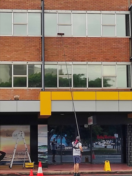 A man using a water-fed pole on the windows of a brick commercial building
