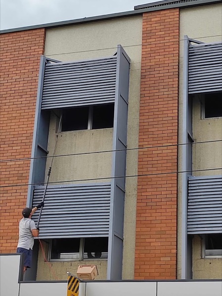 A man on a ladder at the louvred windows of a multi-storey building