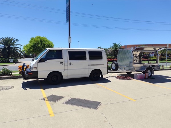 A work van and equipment trailer parked in an open carpark