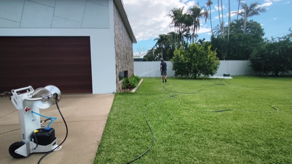 A pressure washing machine set up on a path beside a house