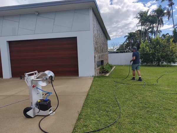 A pressure washing machine on a driveway with a hose running across the lawn