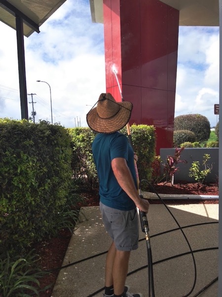 A man holding a hose beside a hedge at a shopfront