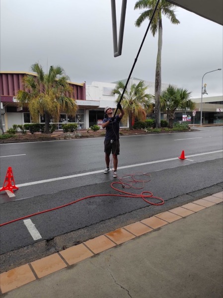 A man using a water-fed pole on a street in Mackay